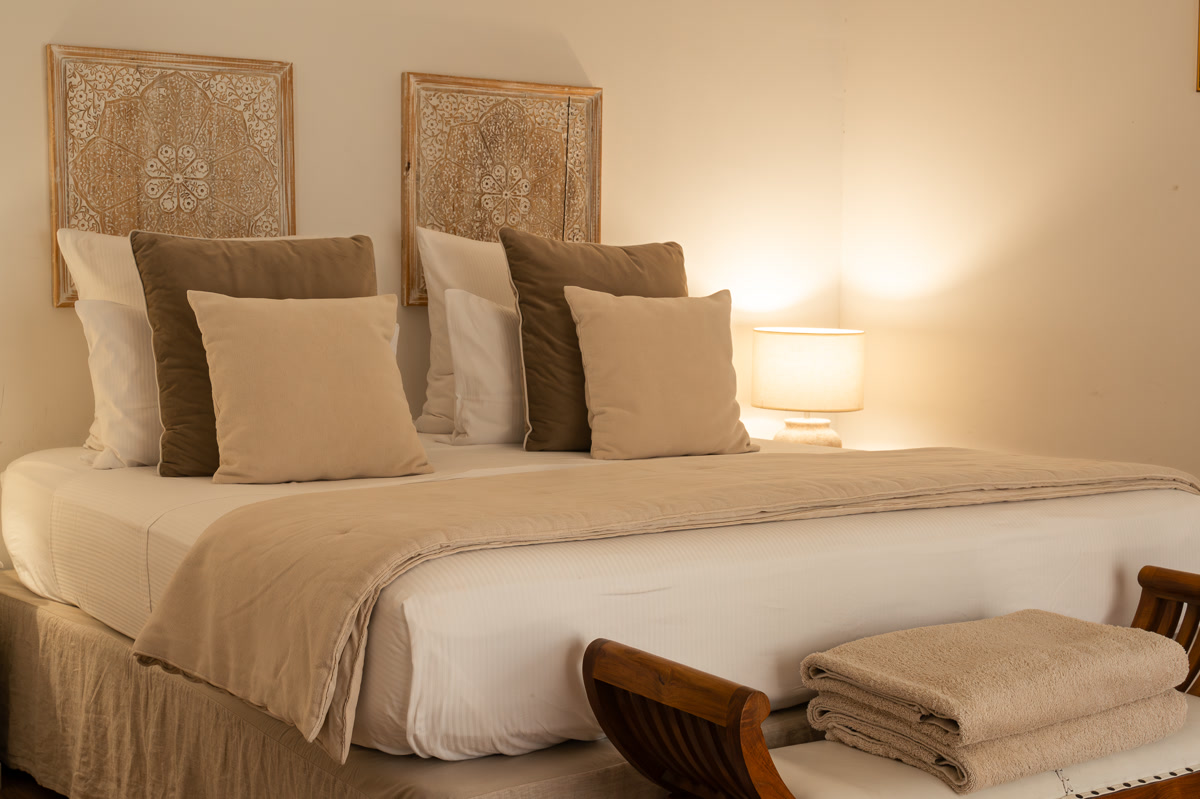 La chambre La Bégude : le lit sous les panneaux de bois sculpté, la lampe et les serviettes pliées