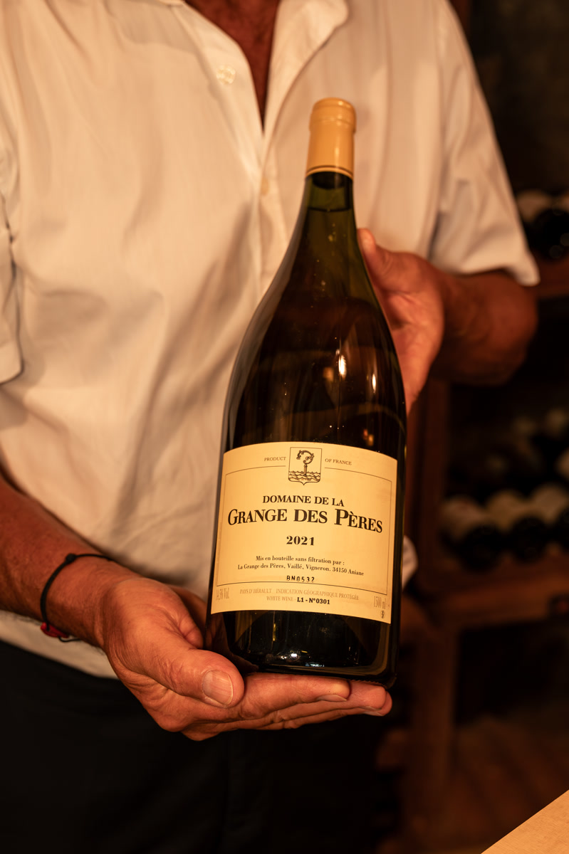 Alain présente une bouteille du Domaine de la Grange des Pères, dans la cave de la maison