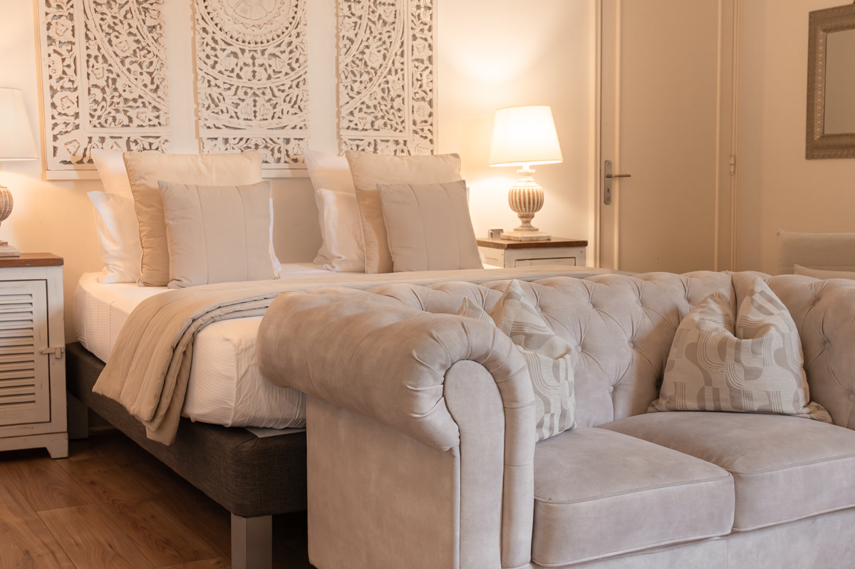 La suite Eldrad : le lit sous les panneaux sculptés blancs, le canapé du salon d'invités au premier plan