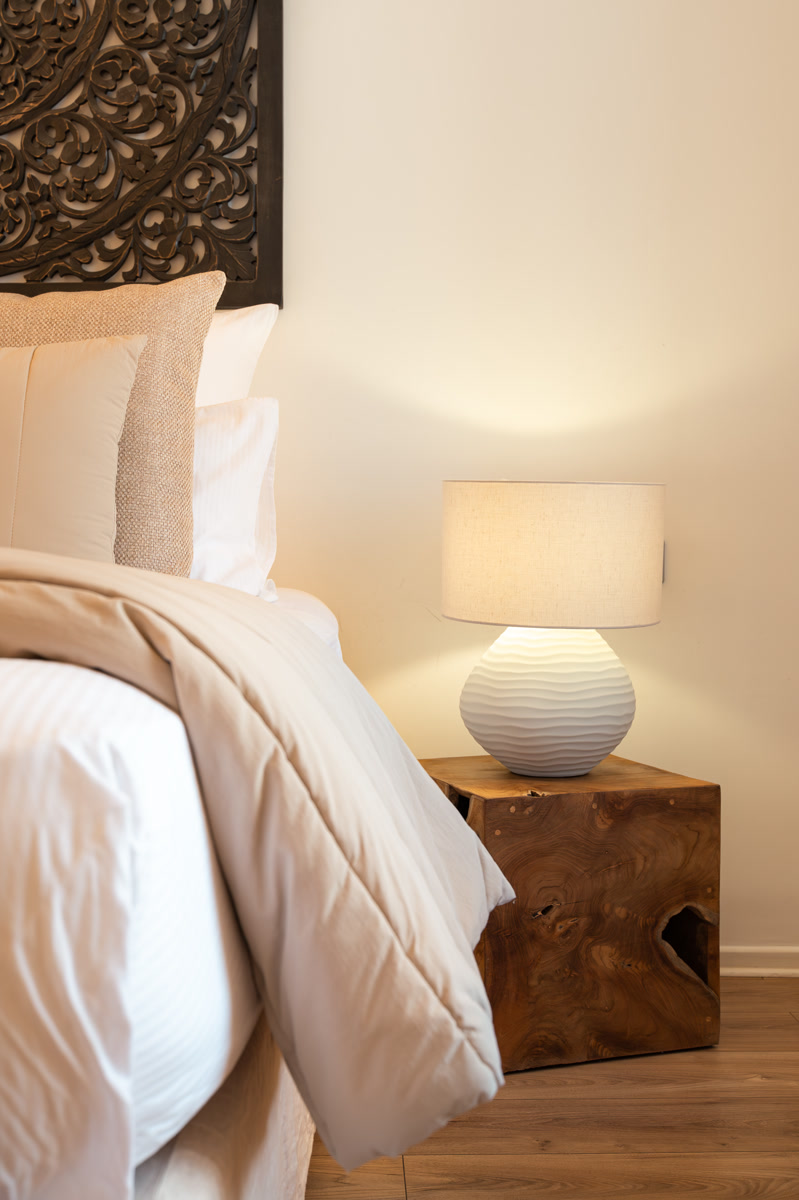 Le chevet en teck brut et sa lampe, à la tombée du jour