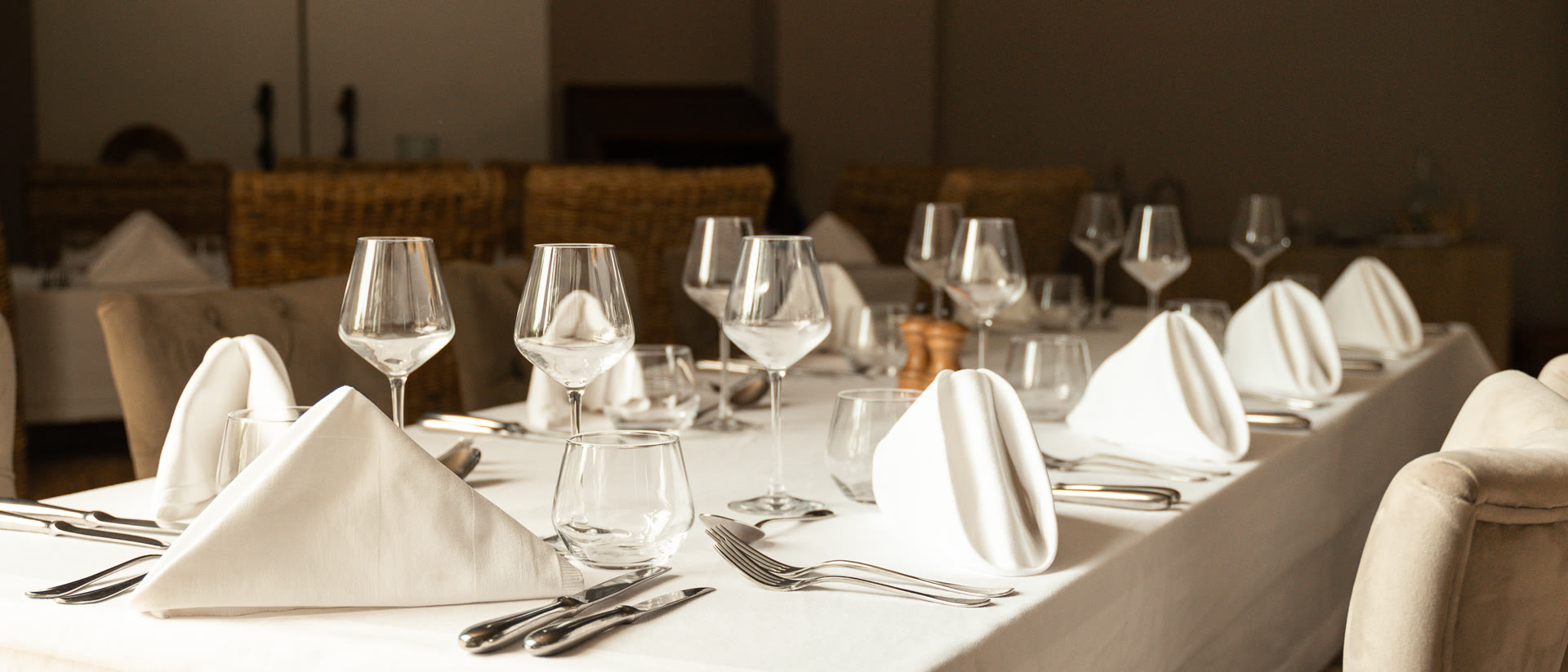 La salle de réception dressée en grande tablée, nappes blanches et verres alignés