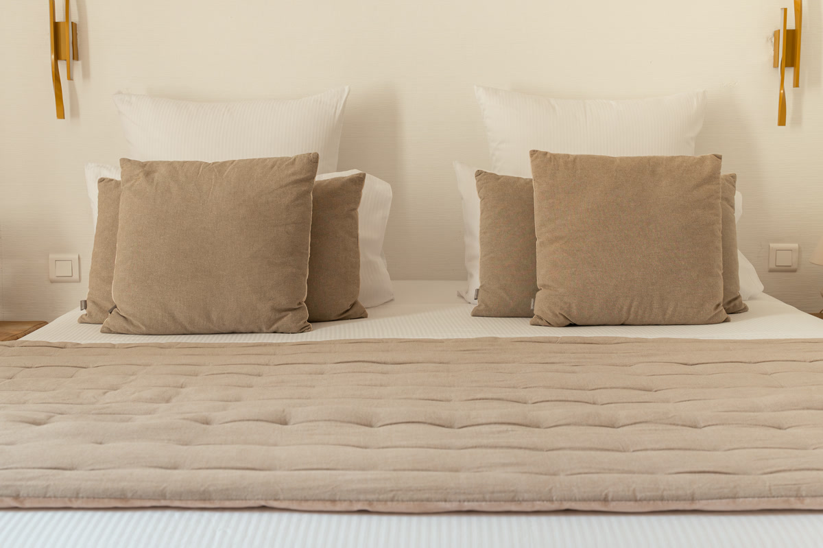 Le lit de La Seuil, coussins taupe et appliques dorées