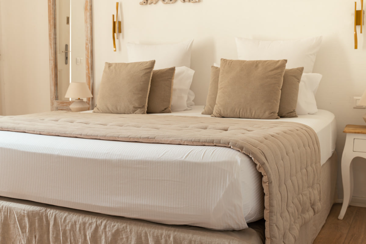 La chambre La Seuil : le lit au plaid beige, les appliques dorées et le miroir ancien