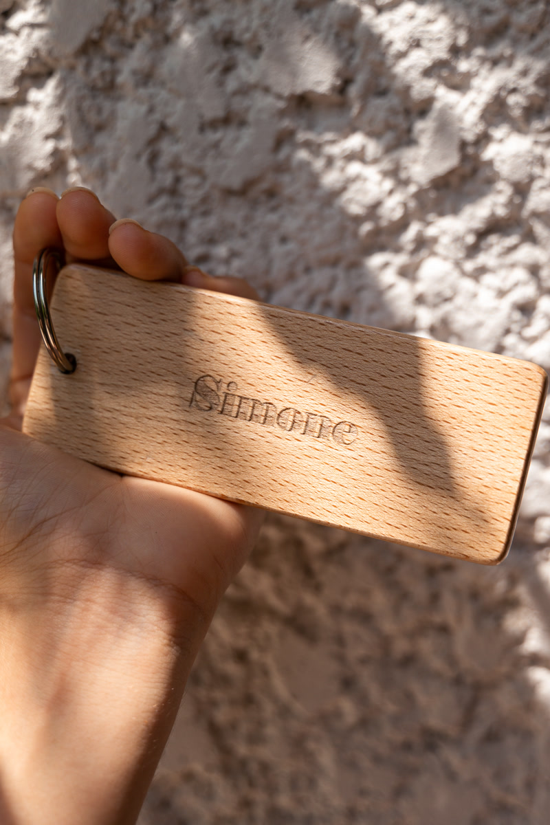 La clé en bois gravée Simone, dans la main devant le mur de pierre