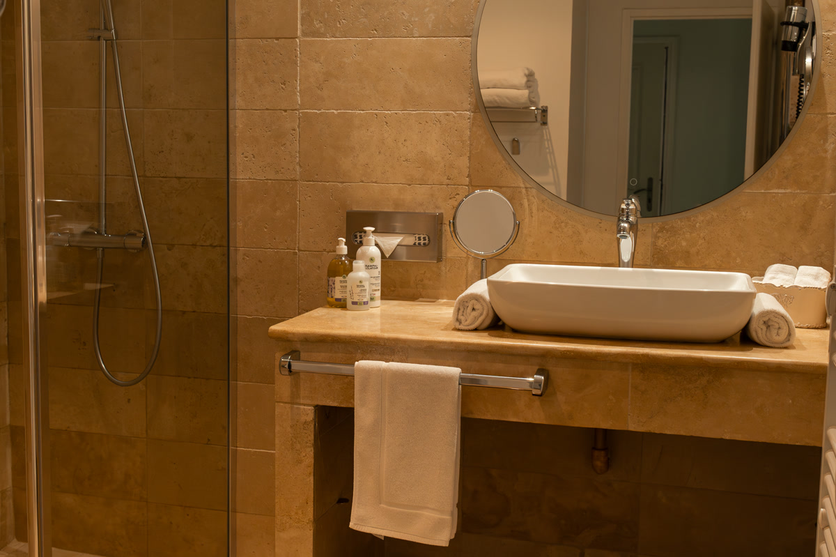 La salle de bain en travertin : douche, vasque et miroir rond