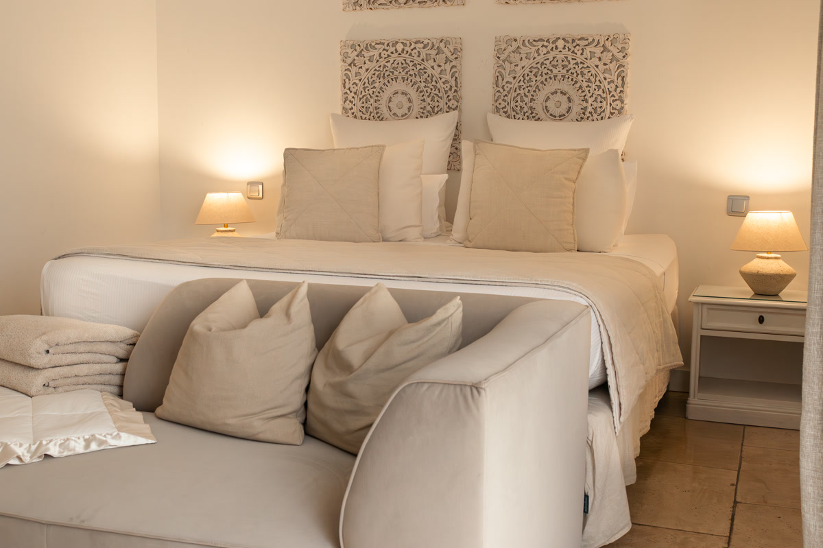 La chambre La Terre Blanche : le lit sous les quatre panneaux sculptés blancs, la banquette au premier plan